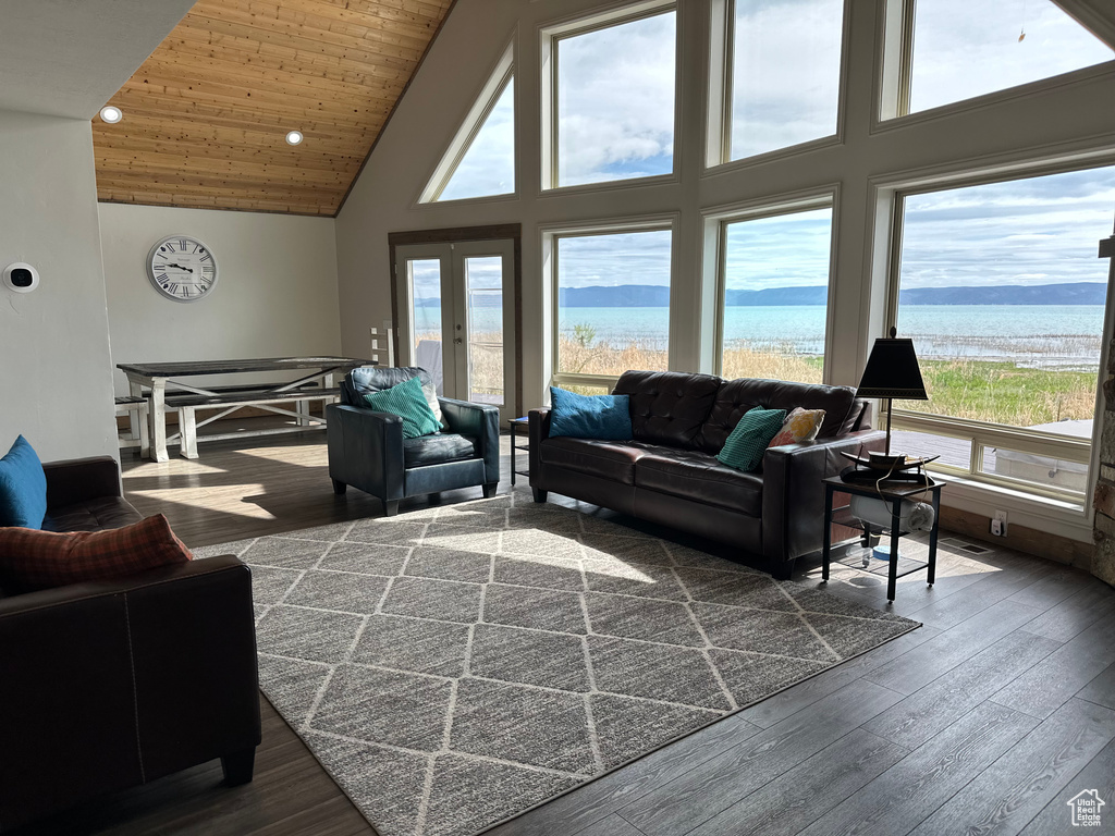 Living area with high vaulted ceiling, a water view, healthy amount of natural light, dark wood finished floors, and wooden ceiling