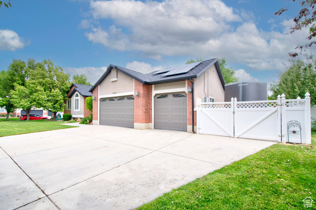 View of side of property featuring a gate, an attached garage, solar panels, driveway, and brick siding