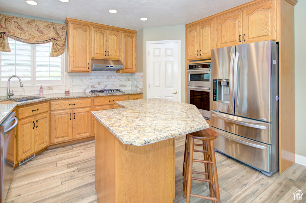 Kitchen featuring appliances with stainless steel finishes, a sink, light wood-type flooring, a kitchen island, and recessed lighting