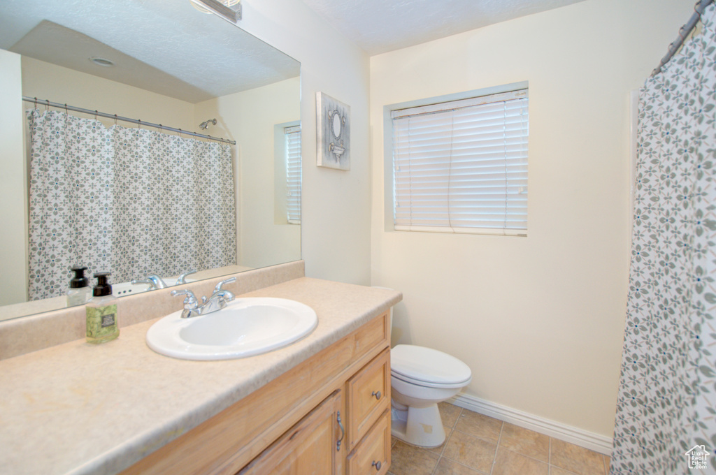 Bathroom featuring toilet, vanity, baseboards, tile patterned flooring, and a shower with shower curtain