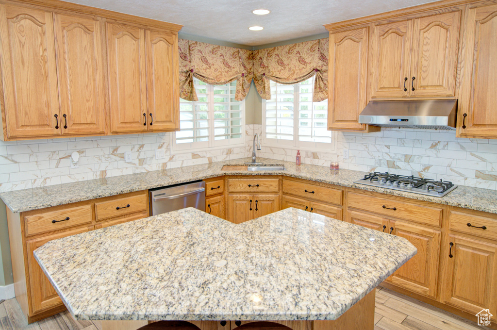 Kitchen with under cabinet range hood, appliances with stainless steel finishes, a sink, light stone countertops, and recessed lighting