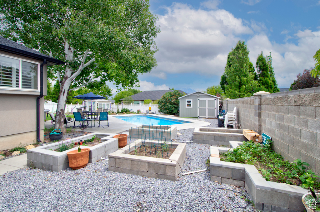 View of swimming pool featuring a garden, a storage unit, a fenced backyard, and an outdoor structure
