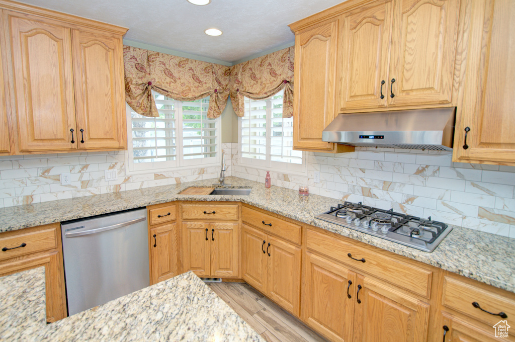 Kitchen with stainless steel appliances, under cabinet range hood, a sink, light stone countertops, and recessed lighting