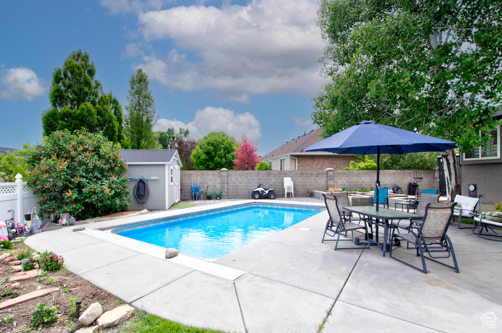 View of pool featuring a patio area, a fenced backyard, a storage unit, an outbuilding, and outdoor dining area