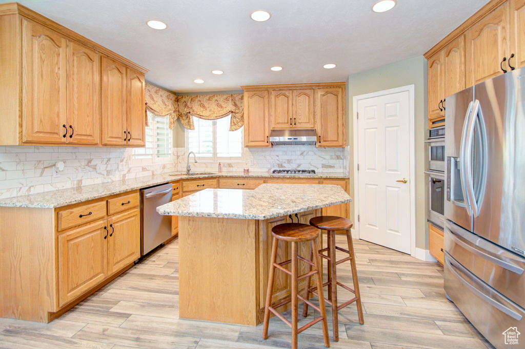 Kitchen featuring appliances with stainless steel finishes, under cabinet range hood, recessed lighting, light stone countertops, and a kitchen breakfast bar