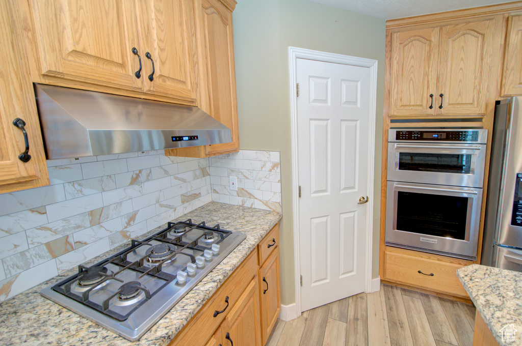 Kitchen featuring under cabinet range hood, appliances with stainless steel finishes, light brown cabinets, and light stone countertops