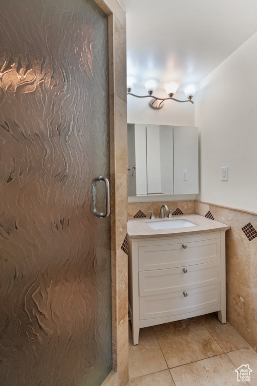Bathroom with tile walls, a shower stall, vanity, and tile patterned flooring