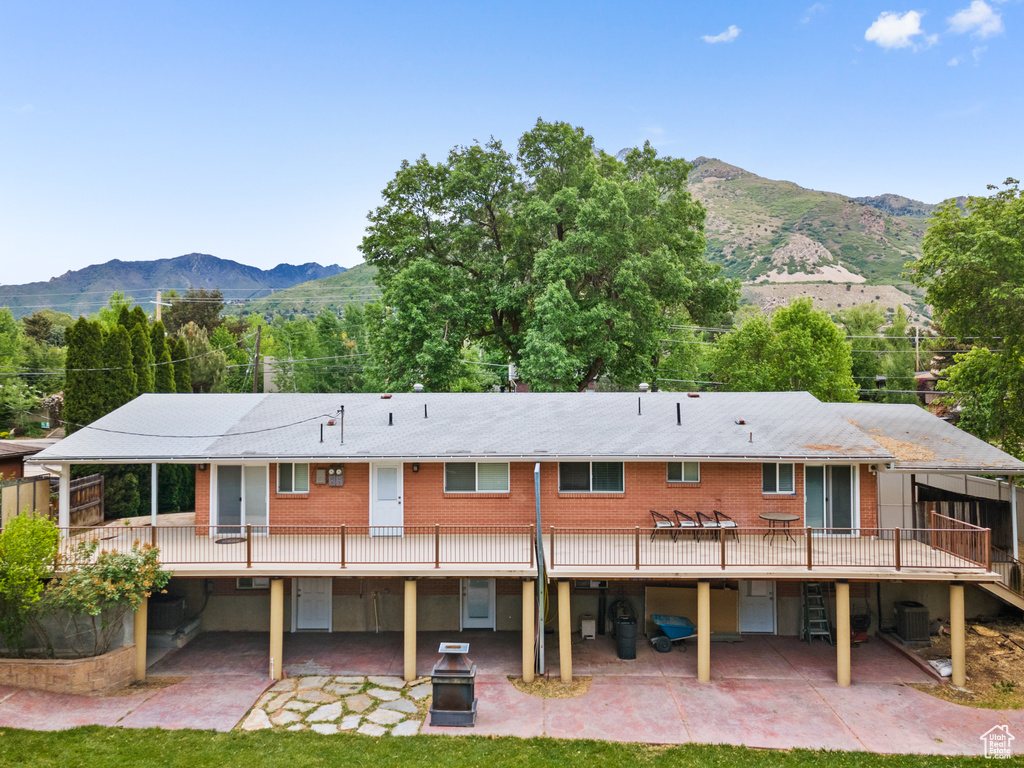 Back of house with a patio, a deck with mountain view, cooling unit, and a yard