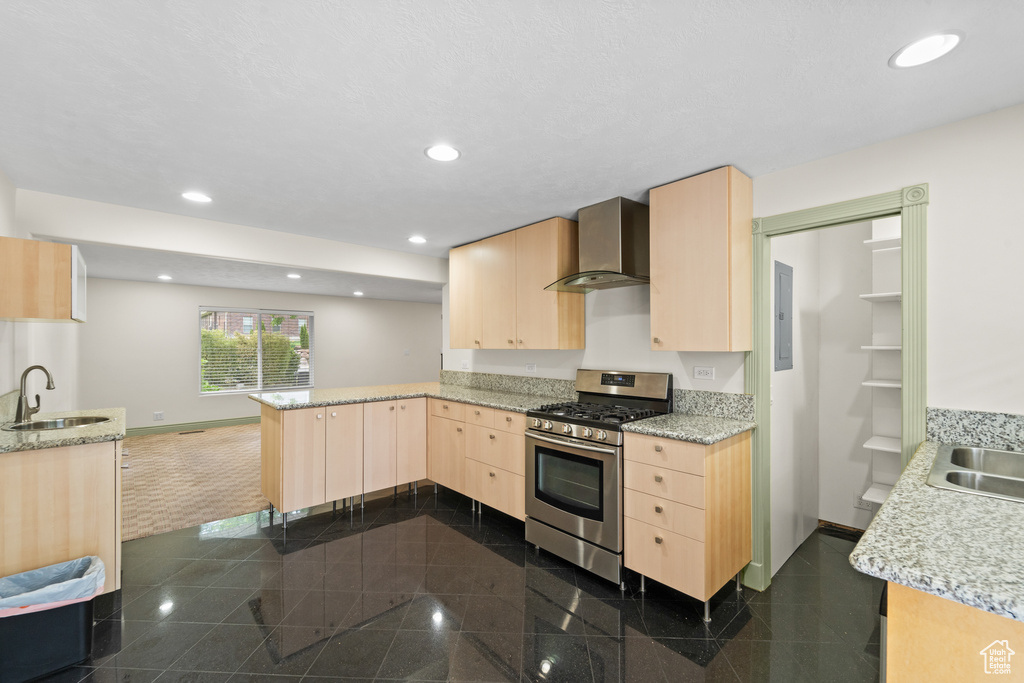 Kitchen featuring gas range, light brown cabinets, wall chimney exhaust hood, a peninsula, and granite tiled floors