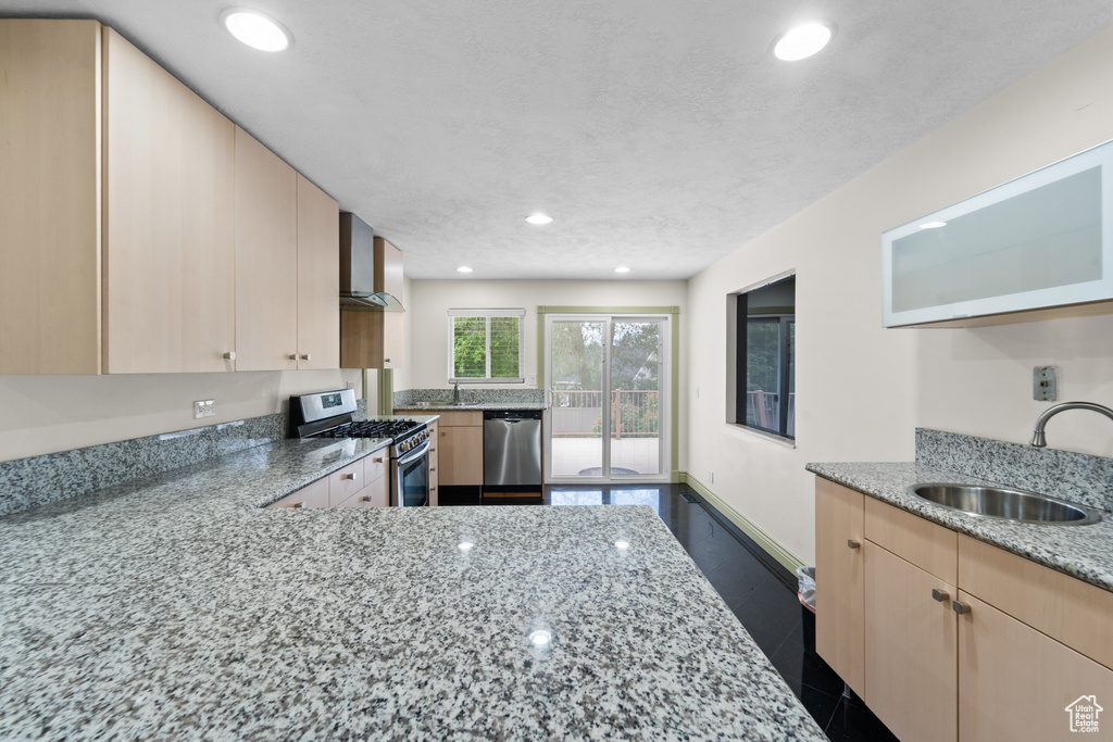 Kitchen with appliances with stainless steel finishes, a sink, light brown cabinetry, wall chimney range hood, and recessed lighting