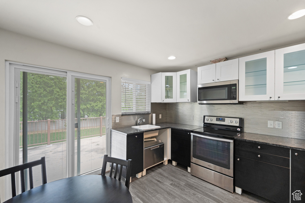 Kitchen featuring appliances with stainless steel finishes, white cabinets, decorative backsplash, light wood finished floors, and a sink