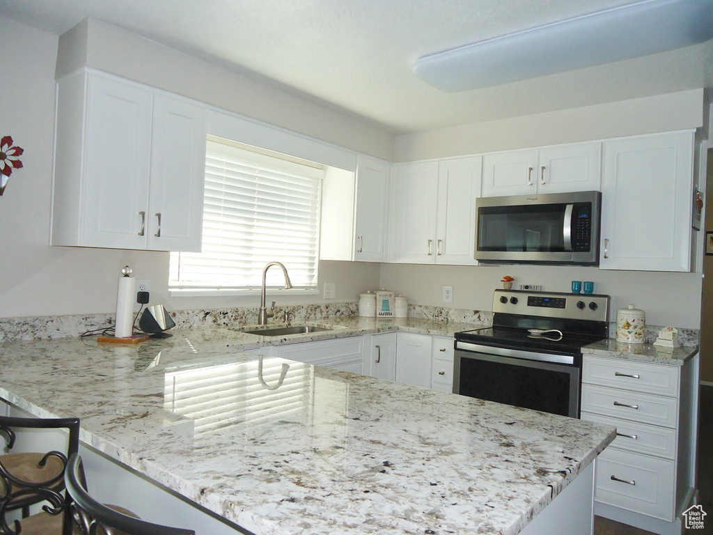 Kitchen featuring appliances with stainless steel finishes, a sink, white cabinetry, a peninsula, and light stone countertops