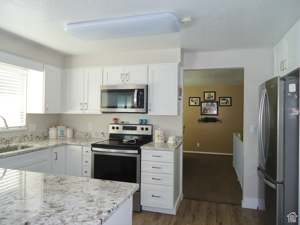 Kitchen featuring appliances with stainless steel finishes, a sink, white cabinets, light stone counters, and dark wood-style flooring