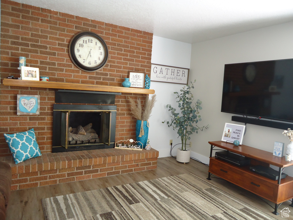 Living room featuring wood finished floors, a brick fireplace, and baseboards