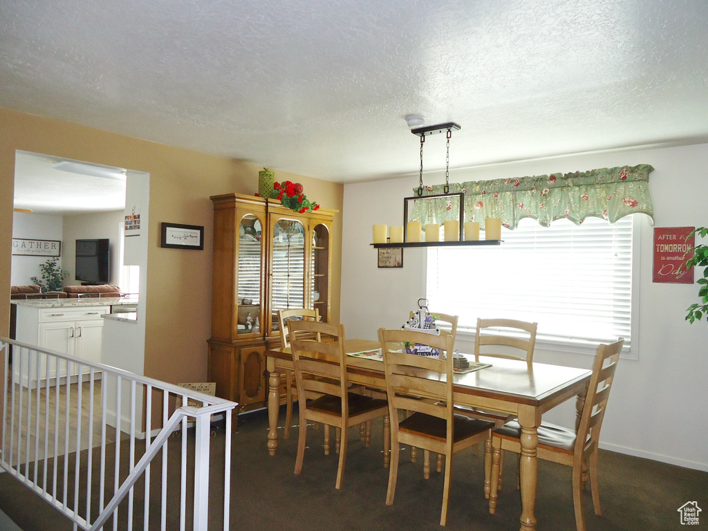 Dining space featuring dark carpet, a textured ceiling, and baseboards