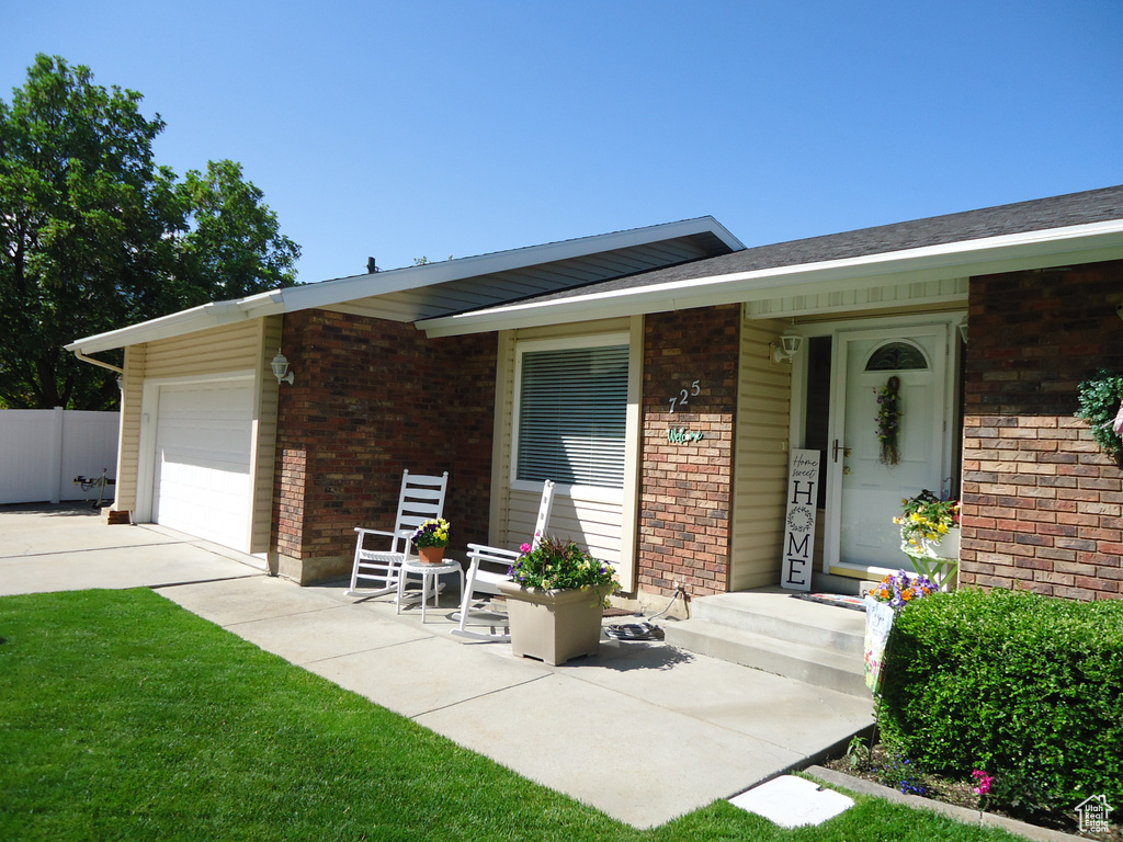 Doorway to property with brick siding, an attached garage, driveway, and fence
