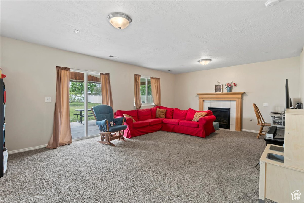 Living room with carpet, a tile fireplace, a textured ceiling, and baseboards