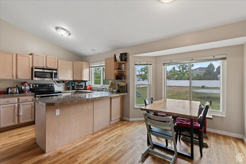 Kitchen with appliances with stainless steel finishes, light brown cabinetry, a peninsula, a sink, and light wood finished floors