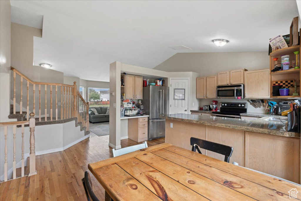Kitchen with appliances with stainless steel finishes, open shelves, light brown cabinets, vaulted ceiling, and light wood finished floors
