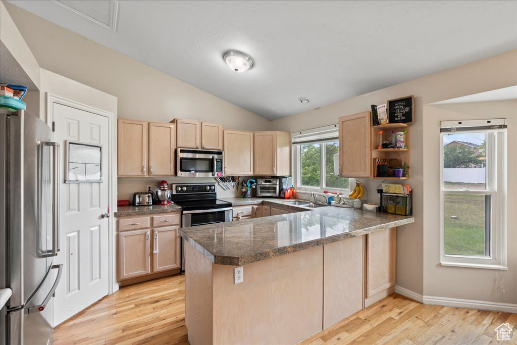 Kitchen featuring appliances with stainless steel finishes, light brown cabinetry, a peninsula, a sink, and light wood finished floors