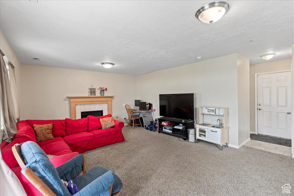 Living room featuring carpet floors, a tiled fireplace, a textured ceiling, and baseboards