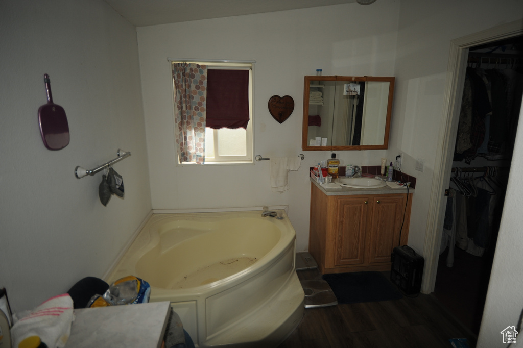Full bath featuring a bath, vanity, a spacious closet, and wood finished floors