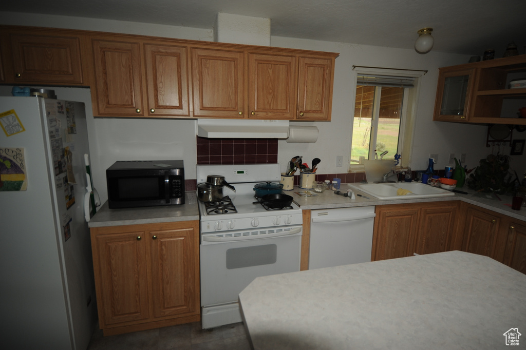 Kitchen featuring white appliances, under cabinet range hood, a sink, light countertops, and brown cabinetry