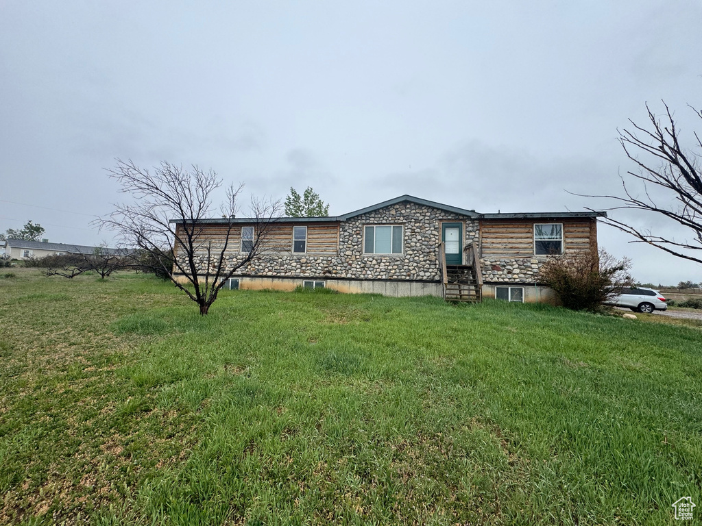 View of front of home with entry steps, stone siding, and a front lawn