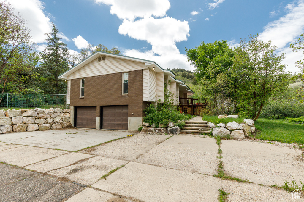 View of property exterior with a garage, brick siding, driveway, and fence