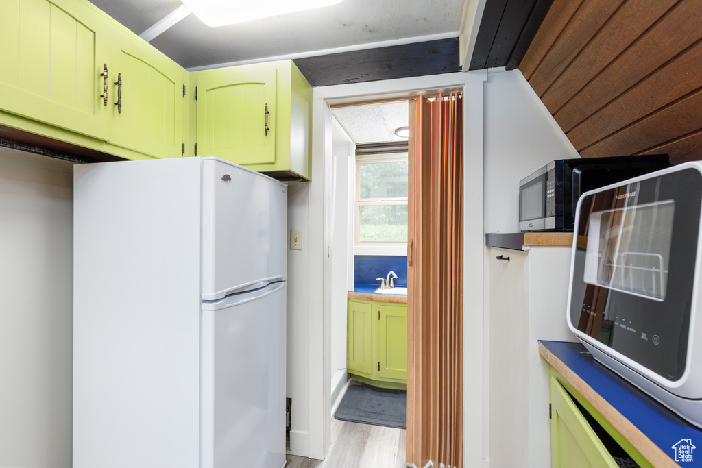 Kitchen with freestanding refrigerator, green cabinetry, and light wood-style flooring