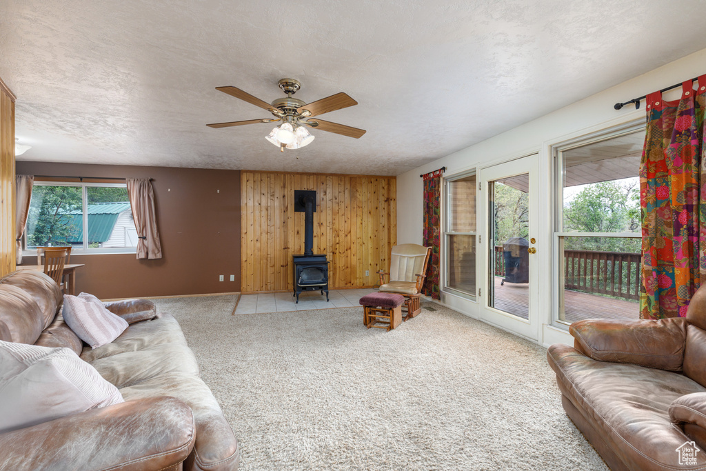 Living room featuring a wood stove, carpet floors, ceiling fan, and wood walls