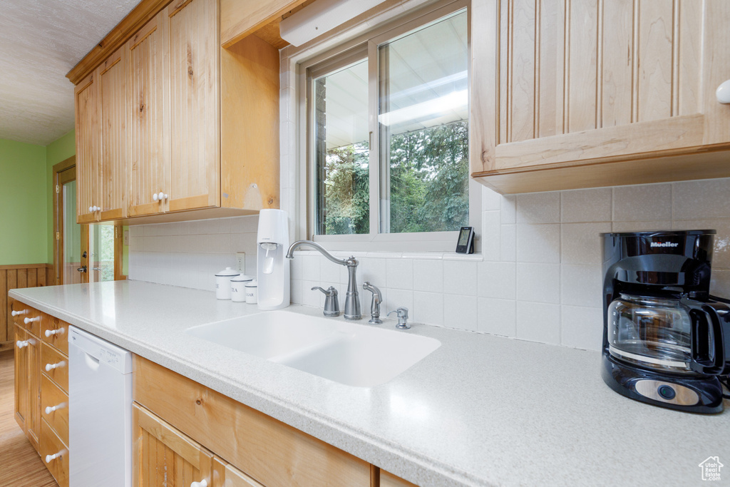 Kitchen with white dishwasher, light countertops, a sink, tasteful backsplash, and wooden walls