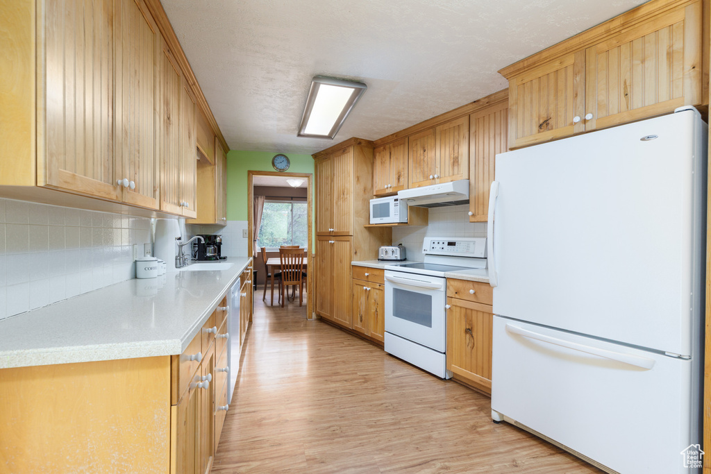 Kitchen featuring white appliances, under cabinet range hood, light wood finished floors, a sink, and tasteful backsplash