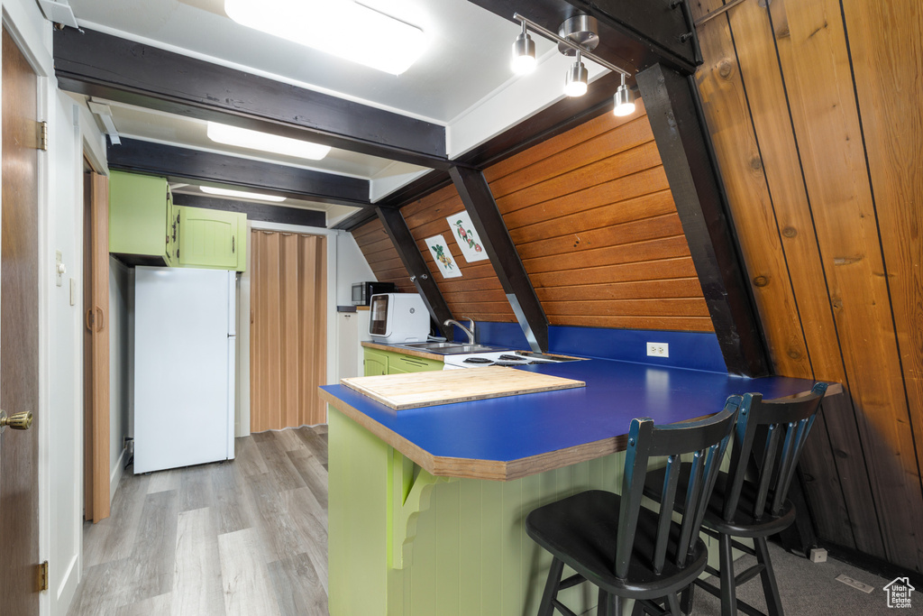 Kitchen featuring freestanding refrigerator, green cabinets, a sink, light wood-type flooring, and a kitchen bar