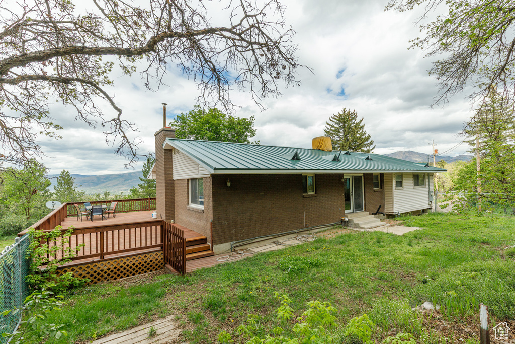 Rear view of property featuring brick siding, a chimney, a deck with mountain view, metal roof, and a lawn