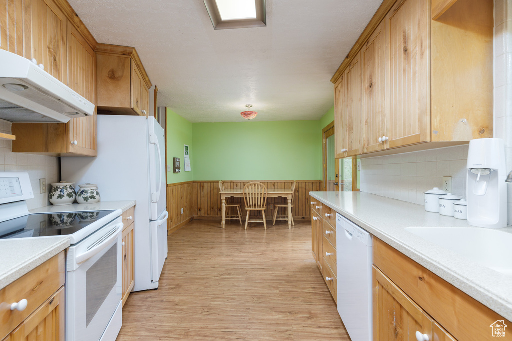 Kitchen with white appliances, under cabinet range hood, light countertops, wainscoting, and light wood finished floors