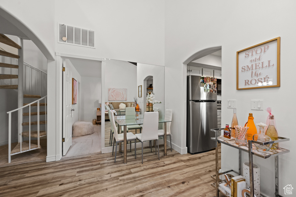 Dining room with wood finished floors, visible vents, stairway, a towering ceiling, and arched walkways