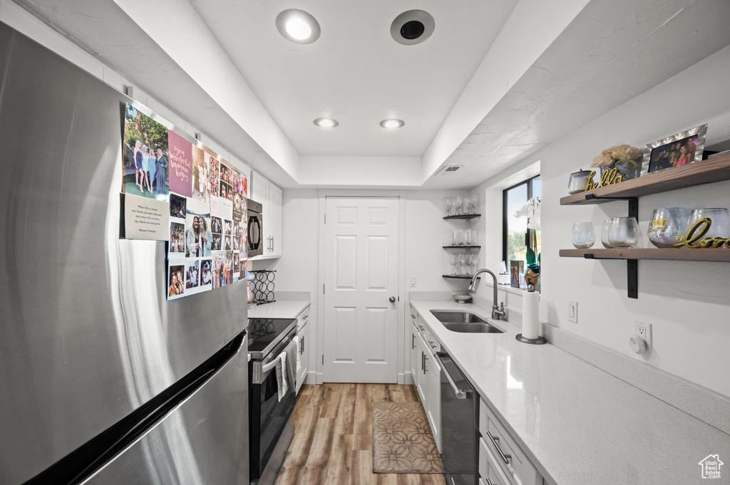 Kitchen with a sink, open shelves, stainless steel appliances, white cabinetry, and light countertops