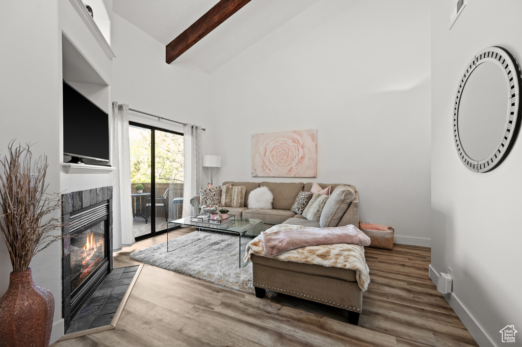 Living area with baseboards, a tiled fireplace, high vaulted ceiling, wood finished floors, and beam ceiling