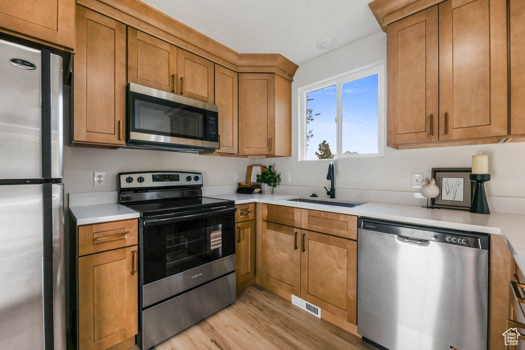 Kitchen featuring stainless steel appliances, a sink, light wood-type flooring, and light countertops