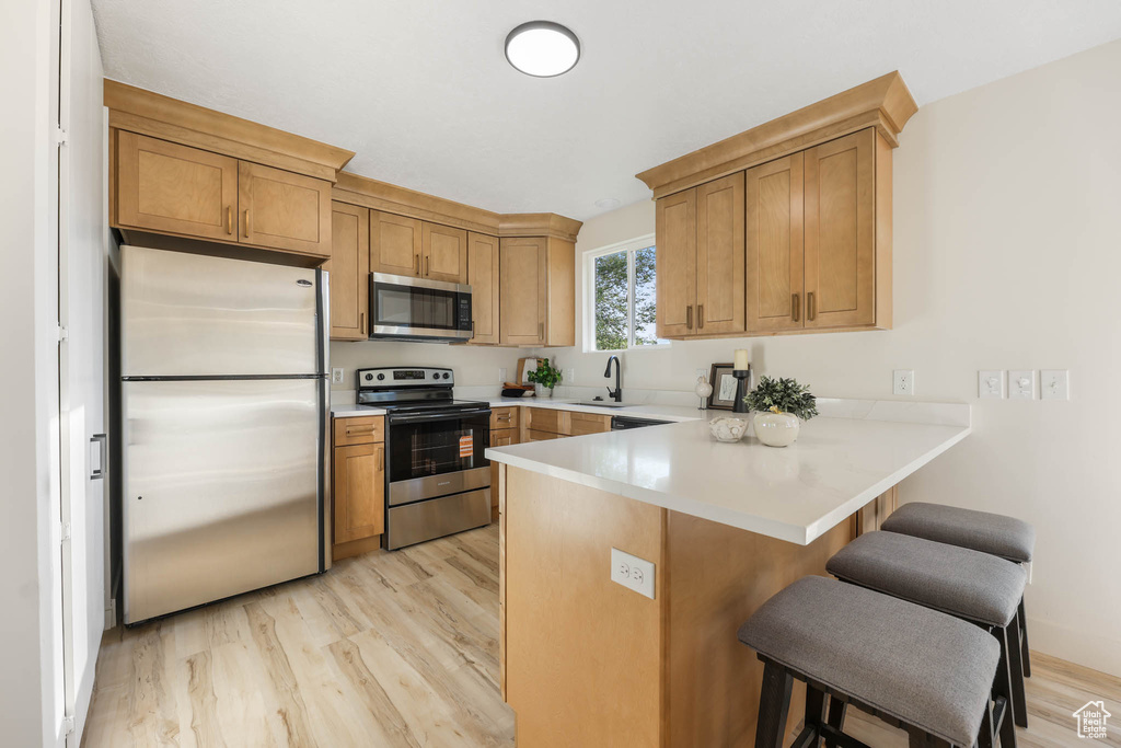 Kitchen with appliances with stainless steel finishes, a sink, a peninsula, and light wood-style floors