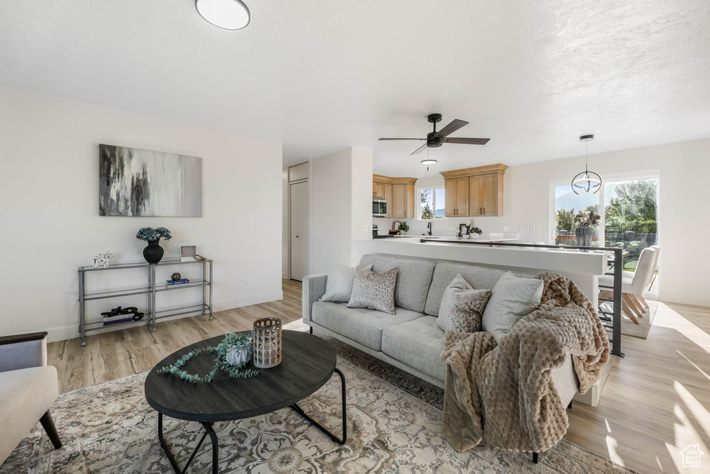 Living area with a ceiling fan, light wood finished floors, and baseboards