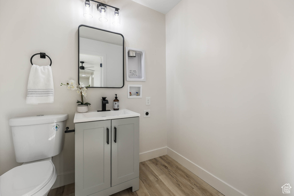 Half bath featuring baseboards, wood finished floors, toilet, vanity, and ceiling fan