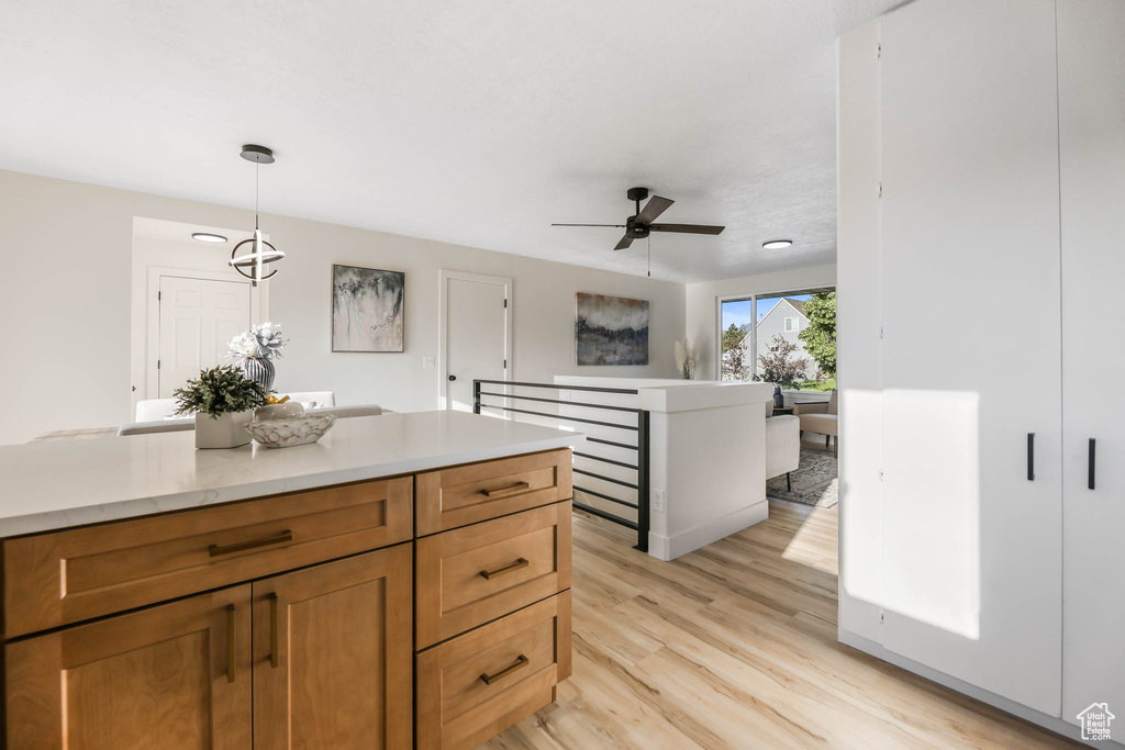 Kitchen featuring light wood-style floors, light countertops, a ceiling fan, decorative light fixtures, and brown cabinets