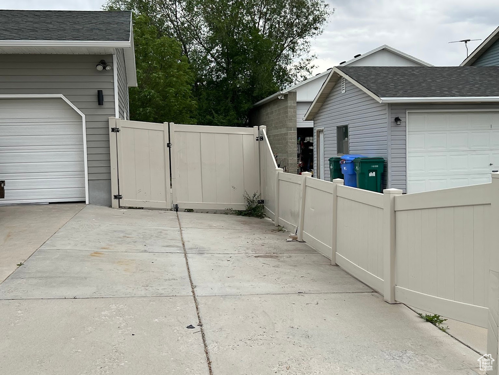 View of side of property with a gate, roof with shingles, fence, and a garage
