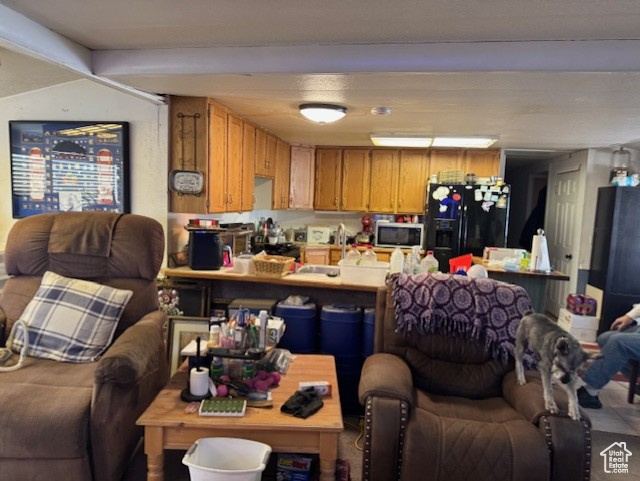Kitchen featuring stainless steel microwave, open floor plan, black fridge, a peninsula, and light countertops