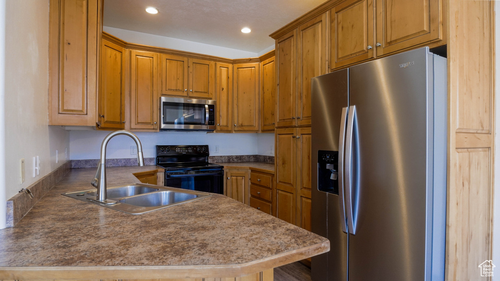 Kitchen with stainless steel appliances, a sink, brown cabinets, recessed lighting, and a peninsula