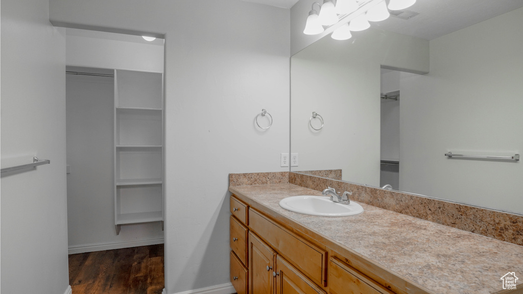 Bathroom featuring wood finished floors, vanity, a chandelier, baseboards, and a walk in closet