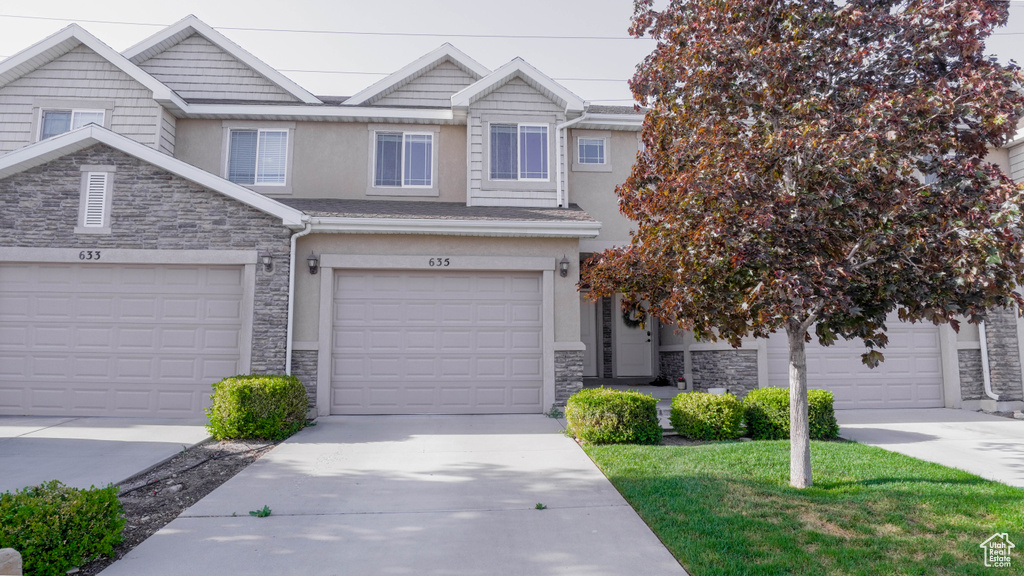 Multi unit property with stone siding, stucco siding, driveway, a garage, and a front lawn