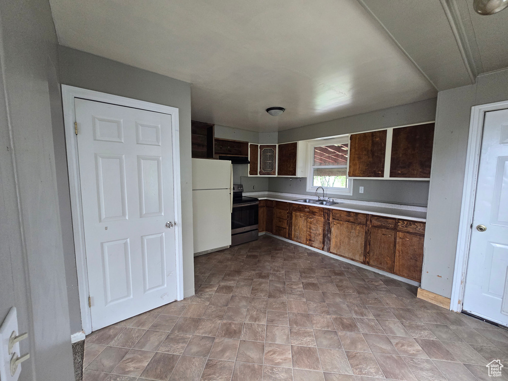 Kitchen featuring stainless steel range with electric stovetop, freestanding refrigerator, a sink, light countertops, and under cabinet range hood